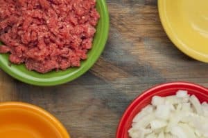 low cholesterol, grass fed, ground buffalo meat and diced onion in colorful ceramic bowls on wood cutting board
